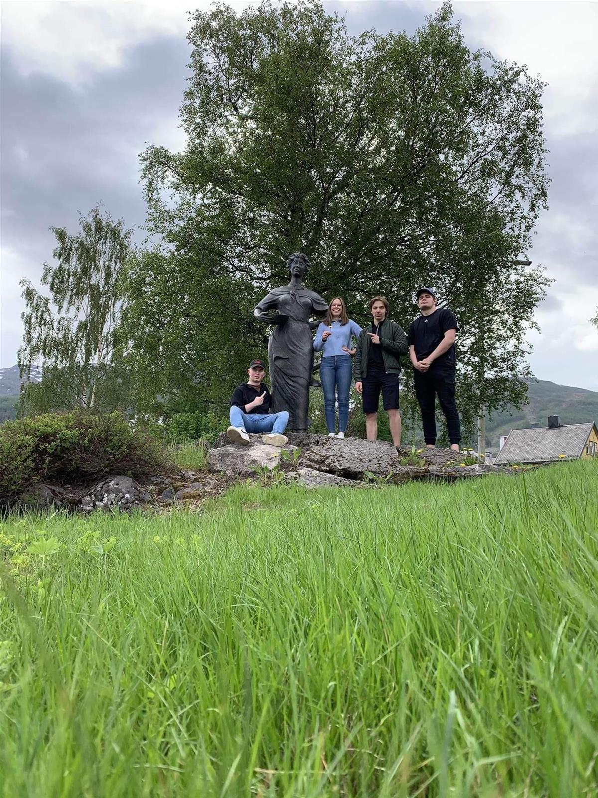Fire elever poserer ved siden av statue i frodig natur i Narvik - Klikk for stort bilde