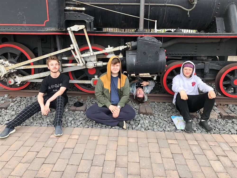 Fire elever sitter foran et gammelt lokomotiv. - Klikk for stort bilde